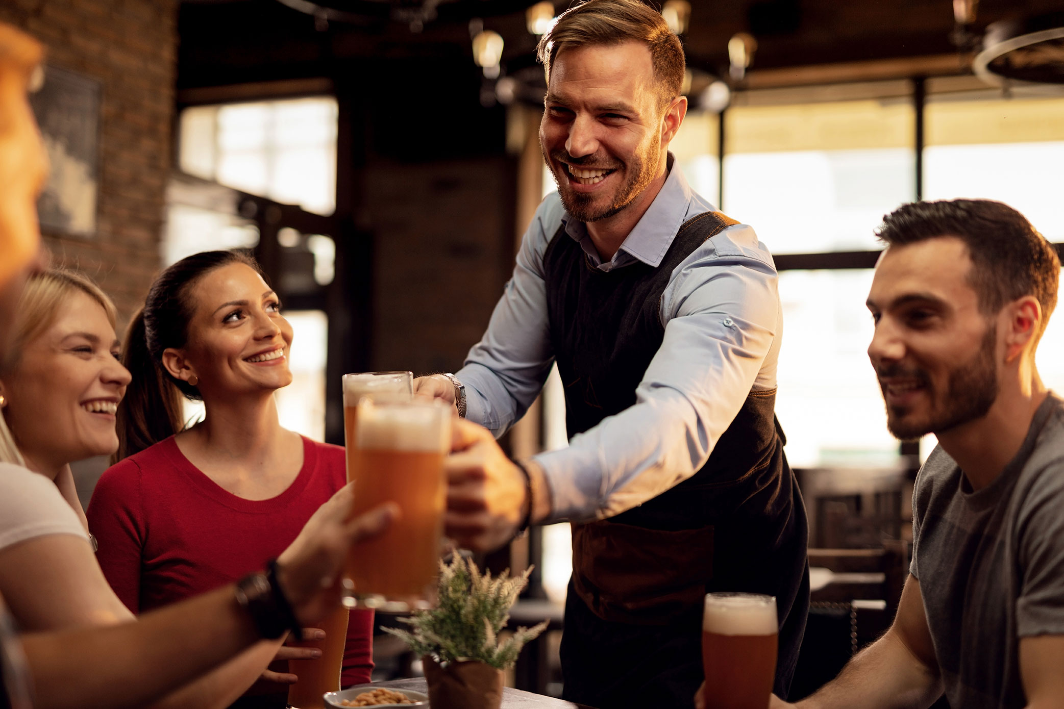 garcom-feliz-dando-cerveja-para-seus-clientes-enquanto-os-serve-em-um-bar